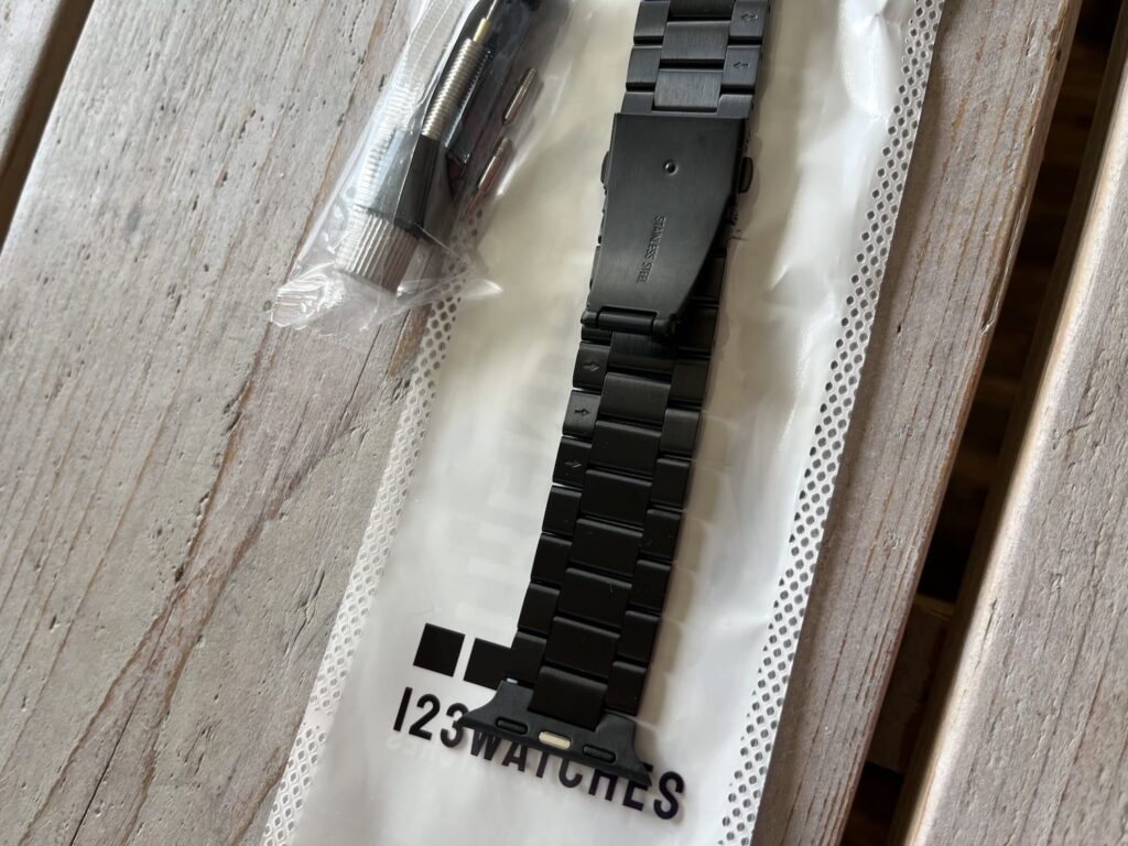 Zijaanzicht van de zwarte roestvrij stalen schakelband van 123watches in de verpakking, met het stainless steel opschrift zichtbaar